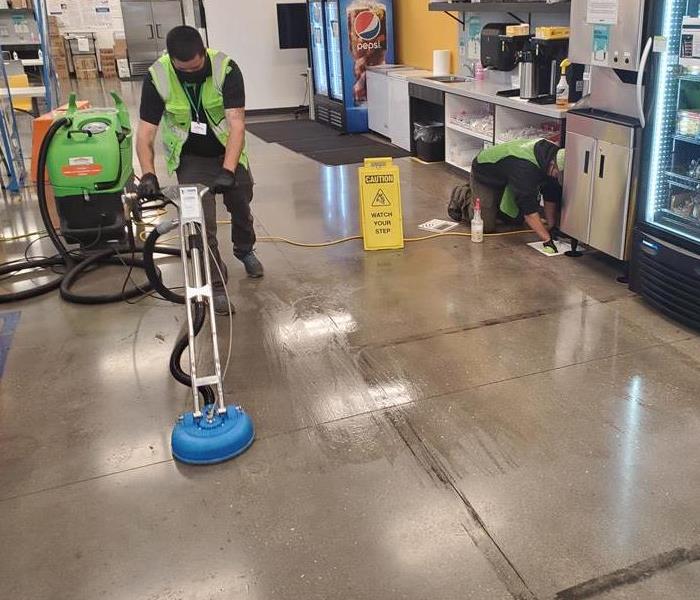 Person using special wand cleaning tool to clean floor in a commercial warehouse